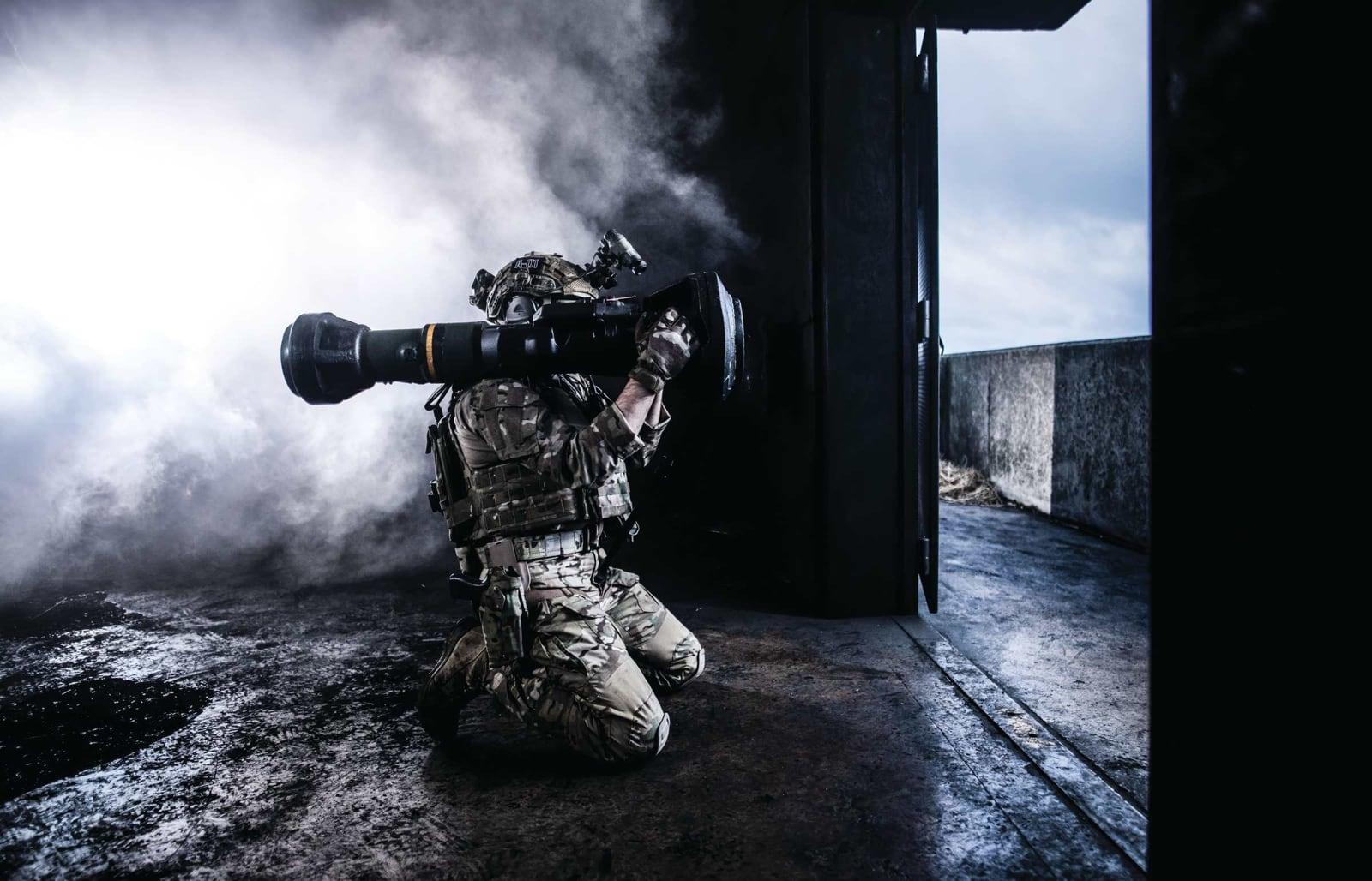 Soldier kneeling in a doorway firing the Carl-Gustaf M4, with backblast smoke