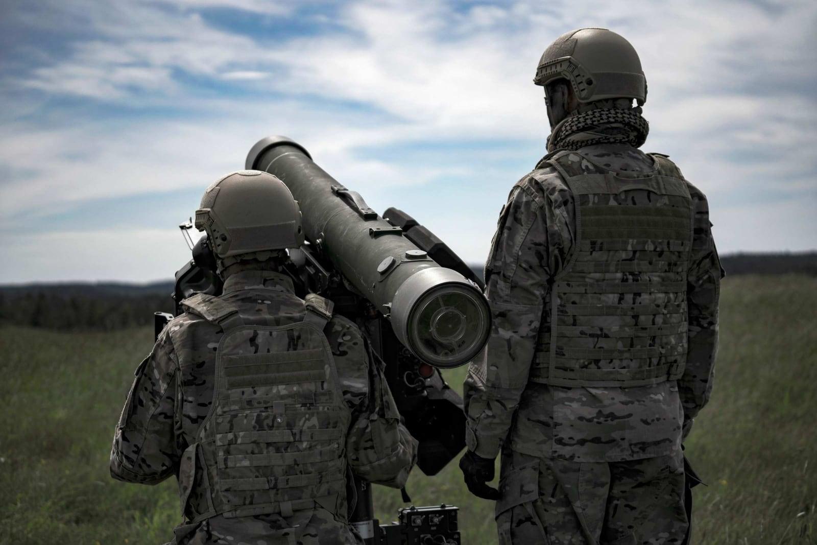 Two soldiers seen from behind in a field, one carrying the Carl-Gustaf M4 on the shoulder