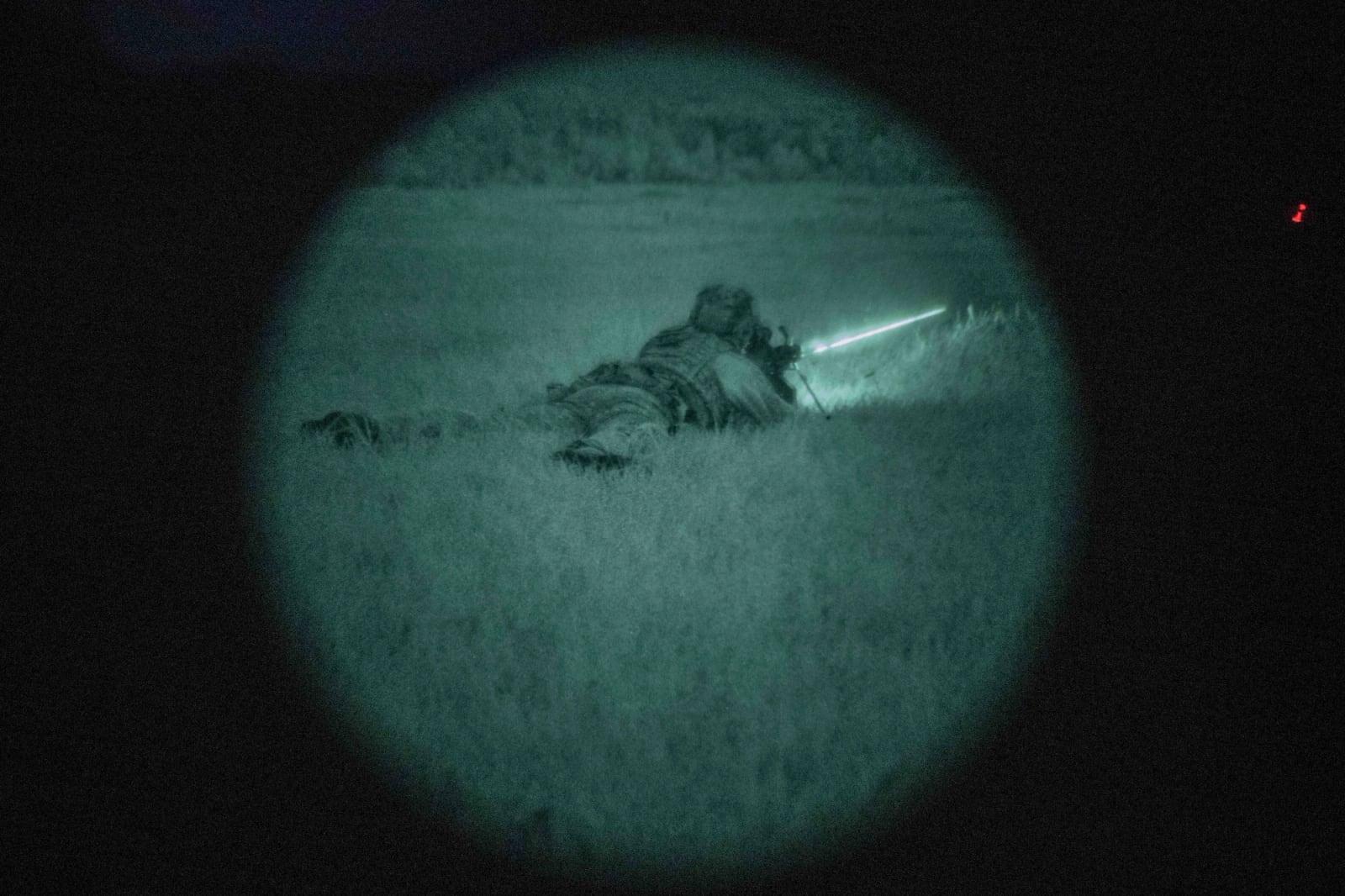 Naval Special Warfare operator firing a Mk 46 MOD 2 light machine gun from the prone position, seen through night vision