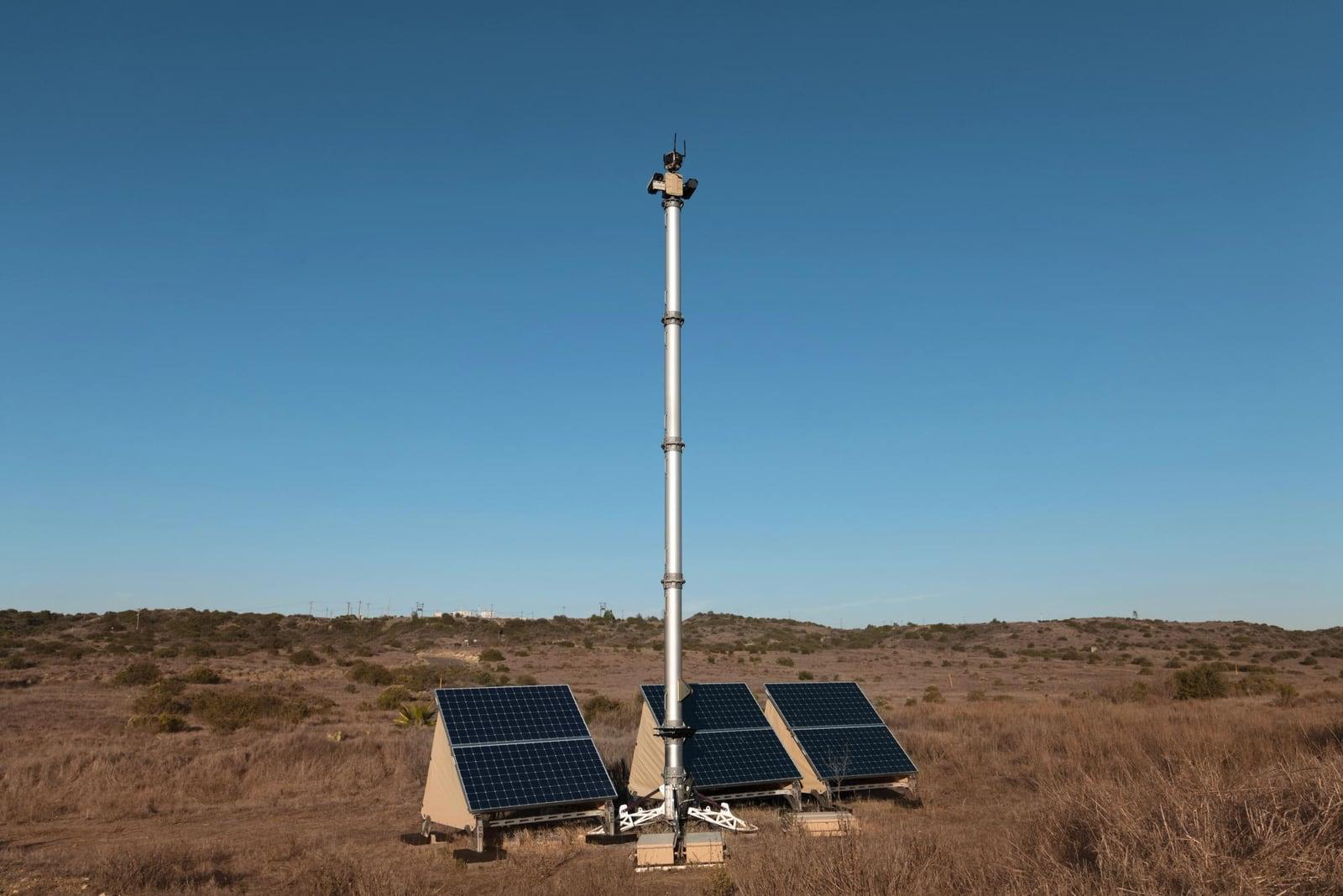 A white sensor mast with three solar panels at its base on a dry hillside